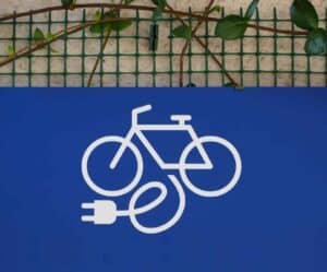 blue ebike charging station sign on a wall with a green wire grid and ivy in background (1)