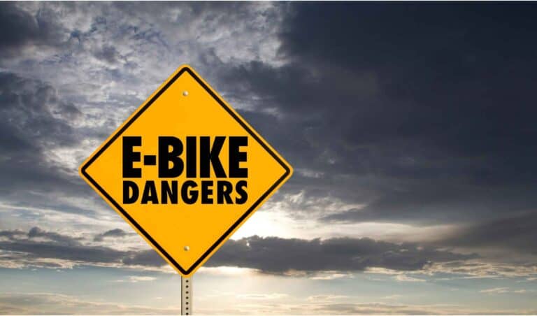 yellow diamond shape sign says e-bike dangers against a grey cloudy sky with sun shining through